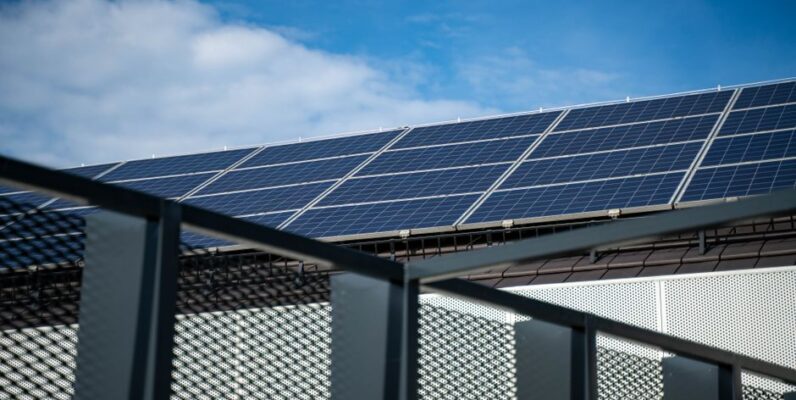 Een afbeelding van zonnepanelen op een dak tijdens een onweersbui met donkere wolken op de achtergrond.